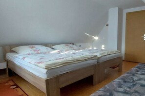 A single bed with a wooden frame and floral bedding in a room with a wooden door and a light fixture on the wall. - Holiday home with 1 bedroom (Bad Gottleuba OT Markersbach)
