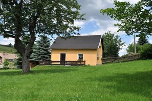 Ein eingeschossiges Haus mit dunklem Dach, einer kleinen Veranda und einem Rasen.