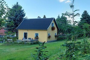 A single-story house with a sloped roof, a front porch with a bench, and a small garden area. - Holiday home with 1 bedroom (Bad Gottleuba OT Markersbach)