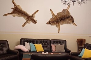 A room with a black leather sofa, a chandelier, and two mounted animal skins on the wall. - Langenthal Forestry House - House II (Braunsroda)
