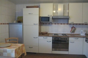 A compact kitchen with white cabinets, a microwave, a stove, and a refrigerator. - Langenthal Forestry Lodge - House I (Braunsroda)