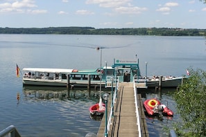 A boat docked at a pier with a view of a calm lake and a forested shoreline. - Holiday home with 2 bedrooms (Klein Nenerow)