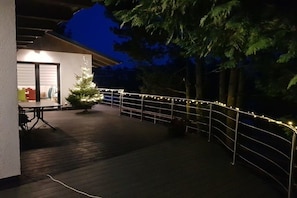 Een terras buiten met een hekwerk, een kleine kerstboom en een tafel met stoelen.