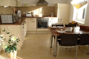 A compact kitchen with a microwave, coffee maker, and oven. There is a dining table with chairs and a potted plant. - "Domizil Fleesensee" (Untergöhren)