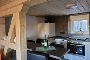 A compact kitchen with a dining area, wooden beams, a built-in oven, and a window with blinds. - Holiday home Unstrutblick (Memleben)