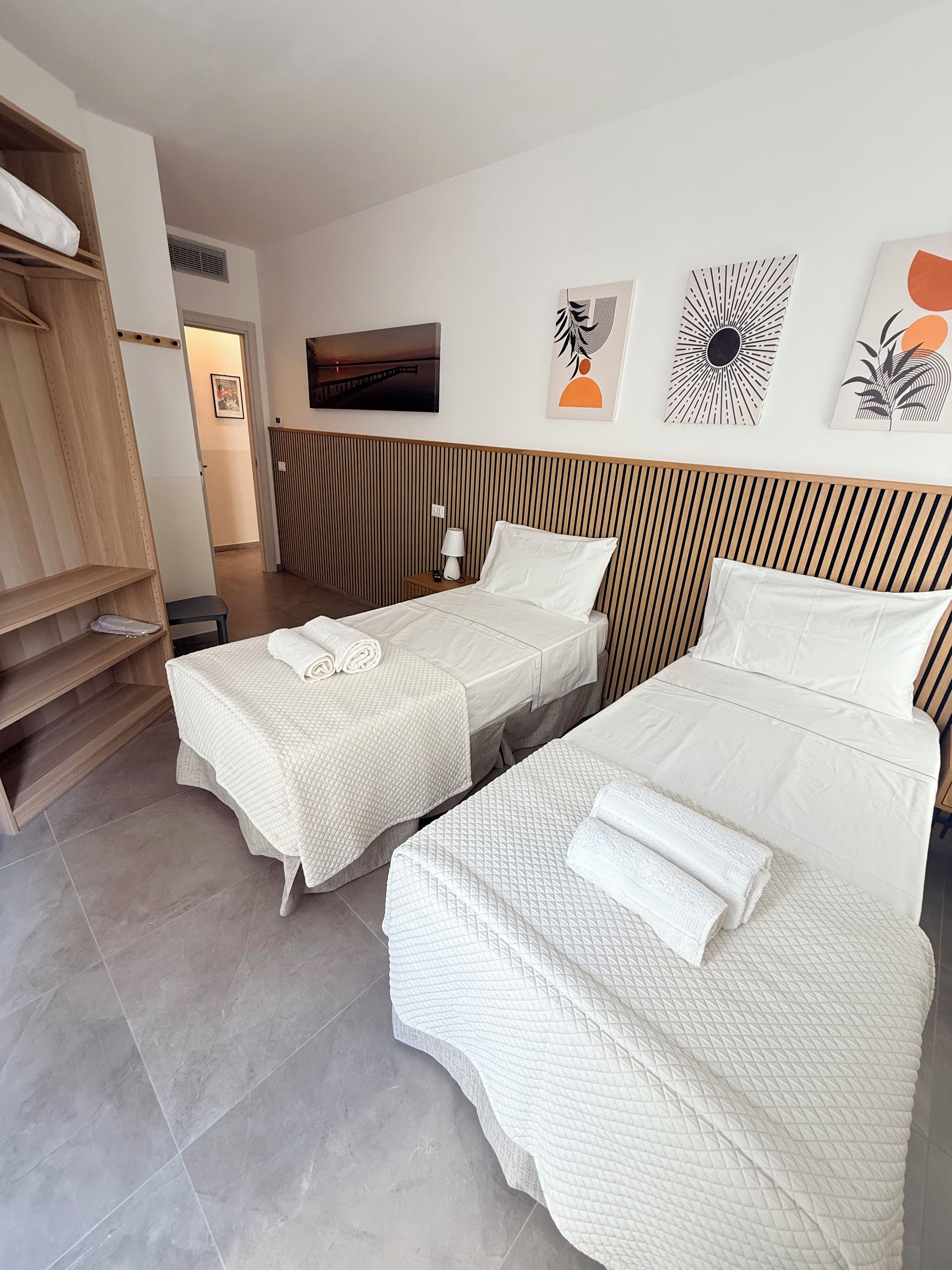 Camera d'albergo con due letti, un armadio in legno, un comodino con una lampada e decorazioni alle pareti.