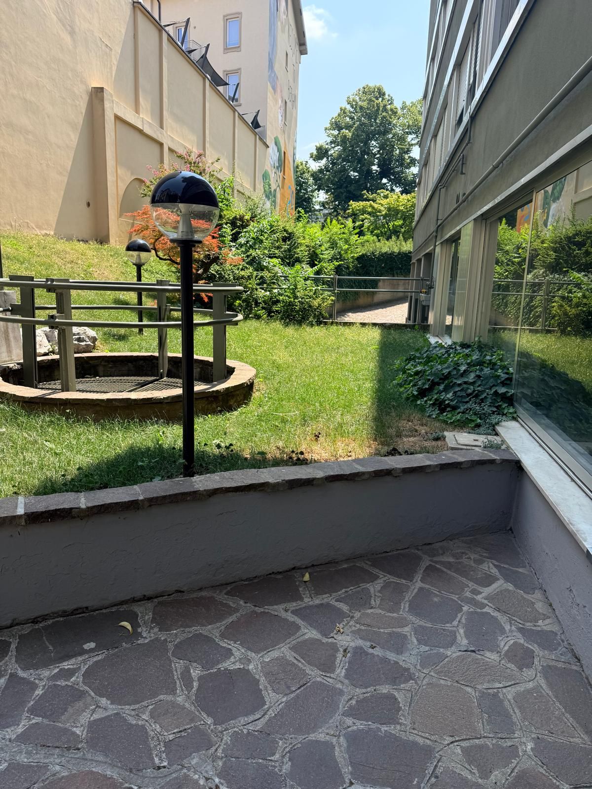 Un cortile con pavimento in pietra, un lampione in metallo e un piccolo giardino a forma circolare.
