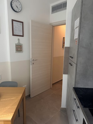 Ein Zimmer mit Holztisch, einer Tür, einer Wanduhr und einem Kühlschrank.