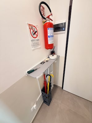 Ein Zimmer mit einem an der Wand befestigten Feuerlöscher, einem kleinen Tisch mit Tablett und einem Kofferständer für Regenschirme.