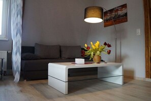 A modern living room with a sofa, a coffee table with a vase of flowers, a lamp, and a painting on the wall. - Holiday apartment with 1 bedroom (Königstein)