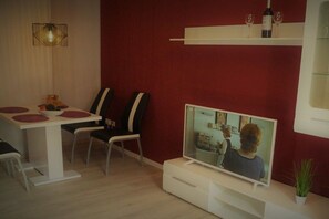 A modern living room with a television, dining area with chairs and a table, and a red accent wall. - Holiday apartment with 1 bedroom (Königstein)