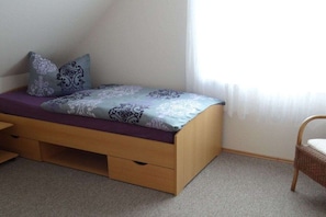 A single bed with a patterned bedspread, a wooden nightstand with drawers, and a wicker chair. - "Little brother"||Schönefeld (Schönefeld)