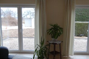 A room with a large sliding glass door leading to a backyard, a potted plant on a small table, and a chair. - "Little brother"||Schönefeld (Schönefeld)