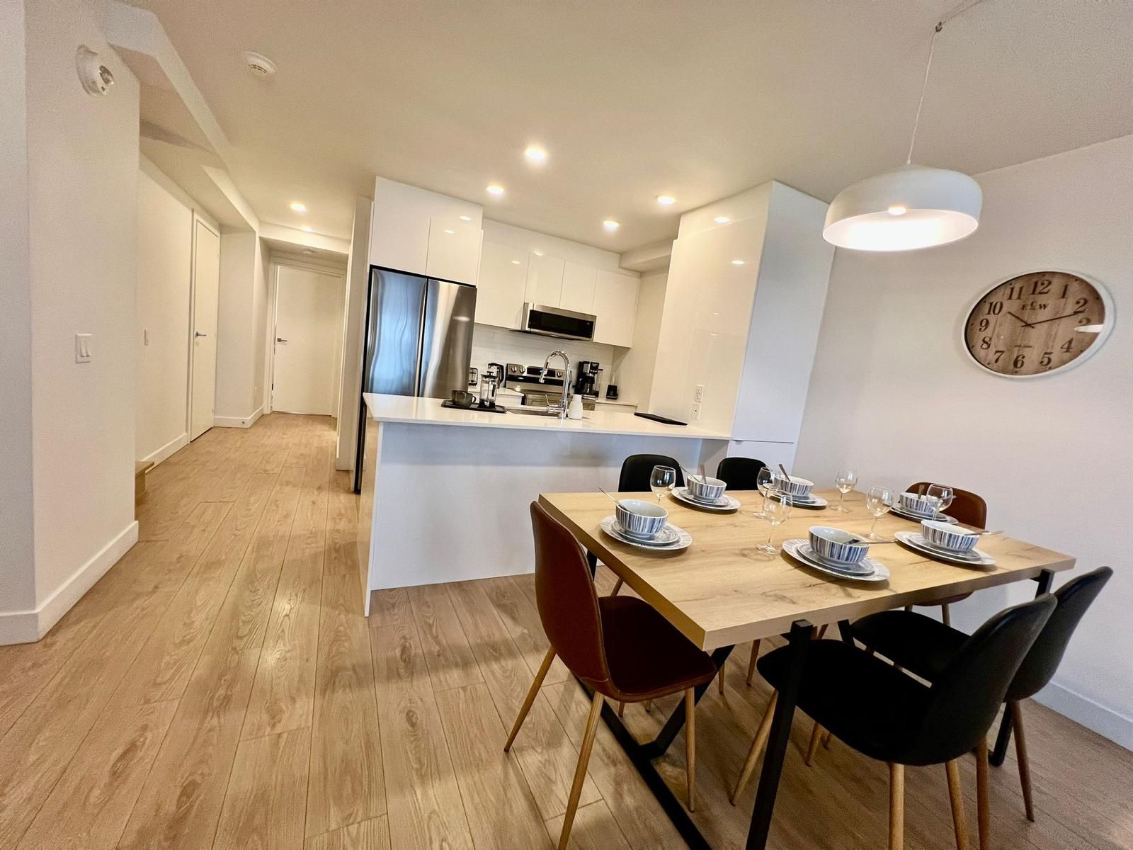 Una cocina moderna con una isla central, mesa de comedor con sillas y un reloj en la pared.