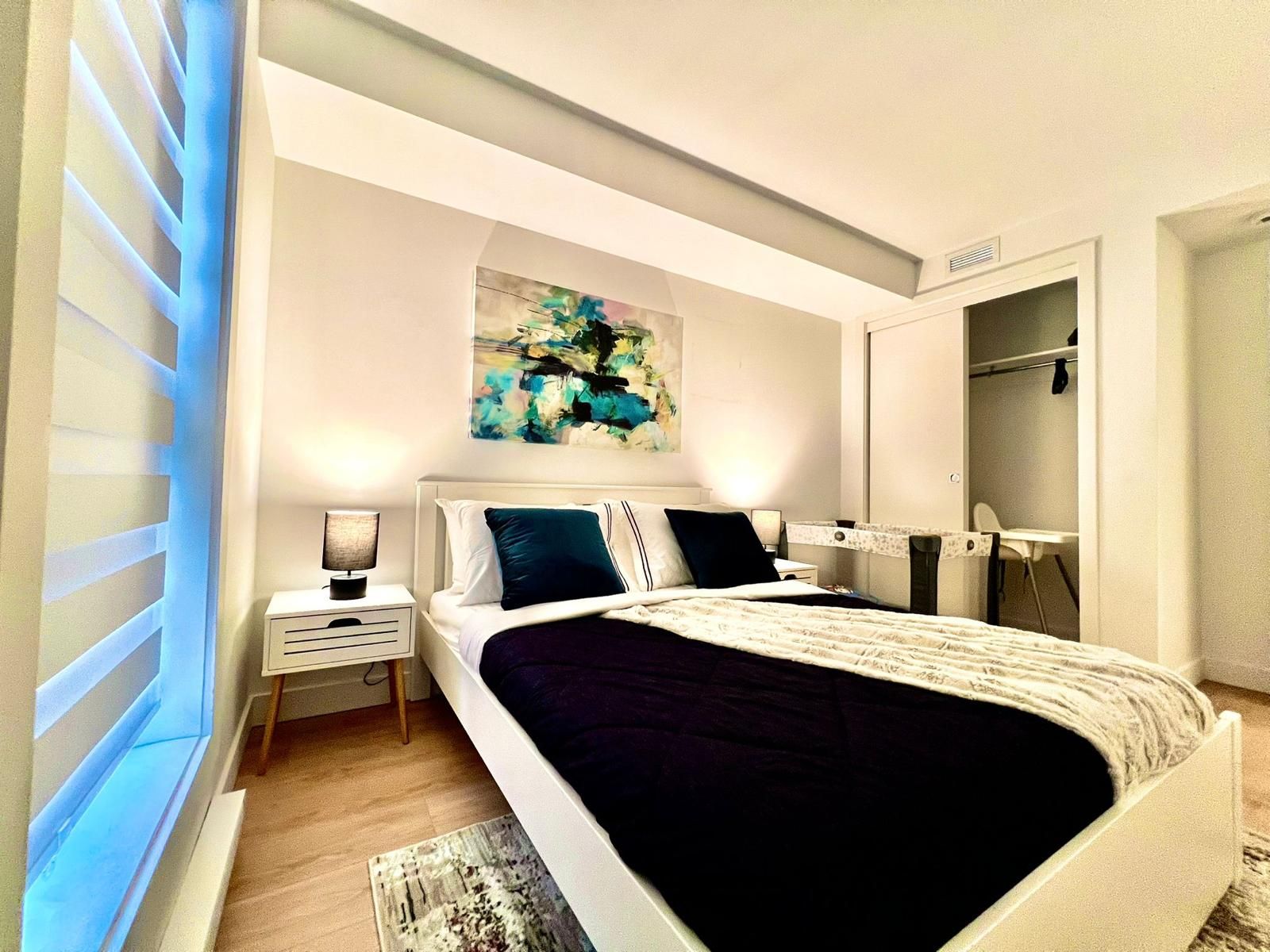 A modern bedroom with a bed, bedside tables, a painting, and a wardrobe.