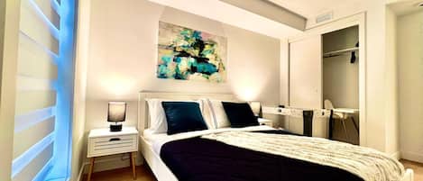 A modern bedroom with a bed, bedside tables, a painting, and a wardrobe.