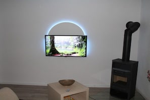 A room with a television mounted on a white wall, a black wood-burning stove, and a small table with a bowl. - Holiday apartment with 1 bedroom (Lohmen)