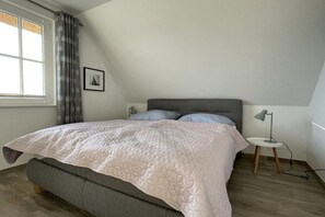 Quarto com cama, abajur, janela com cortinas e um quadro na parede.