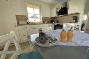 A modern kitchen with white cabinetry, a window, and a dining area with a table set for two. - Thatched house "Three Seagulls" (Zierow)