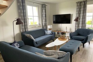 A living room with a sofa, two armchairs, a coffee table, and a flat-screen TV mounted on the wall. - Thatched house "Three Seagulls" (Zierow)