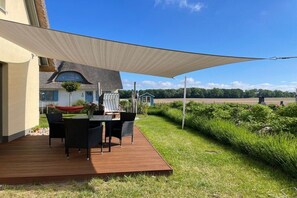 Eine Terrasse mit Gartenmöbeln, ein Gebäude mit Strohdach und Blick auf die Landschaft.