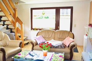 A living room with a sofa, a coffee table, a glass table, a window with a view, and a wooden staircase. - Holiday home in Waren with swimming pool (Waren)
