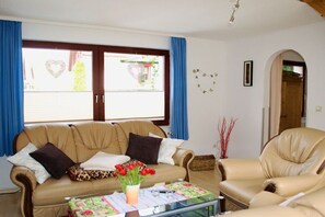 A living room with a sofa, armchair, and coffee table. There is a window with curtains and a view outside. - Holiday home in Waren with swimming pool (Waren)