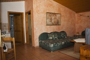Ein Zimmer mit Holzboden, einem grünen Sofa mit Musterbezug, einem Holzschrank und einem Fliesenboden.