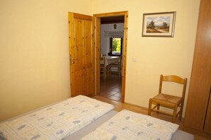 Ein Zimmer mit zwei Betten, einer Holztür, einem Stuhl und einem Bild an der Wand.
