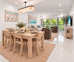 A modern living room with a dining area, featuring a wooden dining table set for four, a sofa, and a television. - Renovated PGA National Home by Guaranteed Rental (Palm Beach Gardens)