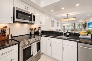 A modern kitchen with white cabinetry, a stainless steel range, a built-in microwave, and a black granite countertop. - Renovated PGA National Home by Guaranteed Rental (Palm Beach Gardens)