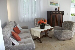 Uma sala de estar com sofá, duas poltronas, uma mesa com um vaso de flores, um armário e um quadro na parede.