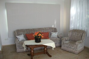 A living room with a sofa, armchair, and a small table with a vase of flowers. - Holiday apartment with 1 bedroom (Dresden OT Borthen)