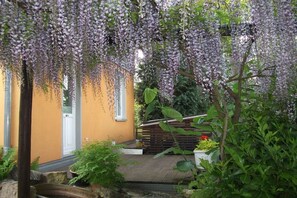 A garden with a wooden deck, a yellow wall, and purple flowering vines. - Holiday apartment with 1 bedroom (Dresden OT Borthen)