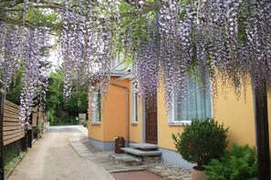 A pathway leading to a yellow building with a wooden fence on one side and a hanging flower display above. - Holiday apartment with 1 bedroom (Dresden OT Borthen)