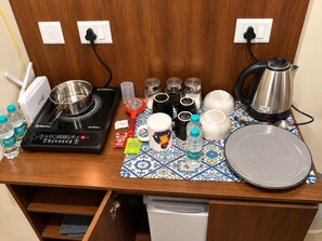 Une petite cuisine équipée d’une cuisinière, d’une bouilloire, d’une machine à café, ainsi que de différentes tasses et mugs.