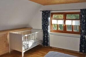 A room with a wooden crib, a radiator, and a window with curtains. - Finsterbusch's little house (Oelsnitz\/Vogtland)