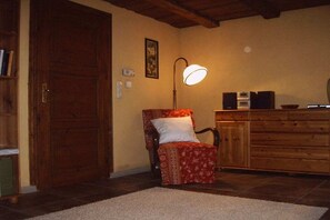 Ein Zimmer mit Holztür, einem gemusterten Sessel, einer Lampe, einem Schrank und einem Fliesenboden.