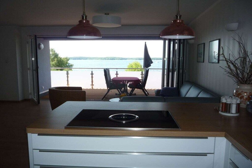 A modern kitchen with a view of a lake, a dining area with a table and chairs, and pendant lights.