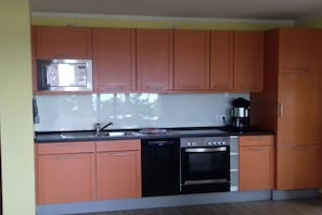 Una cocina con armarios de madera, microondas, cafetera, lavavajillas y horno.