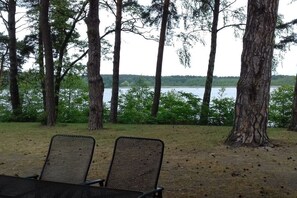 Vista de um lago com árvores ao fundo, duas cadeiras de rede em primeiro plano e um céu limpo.