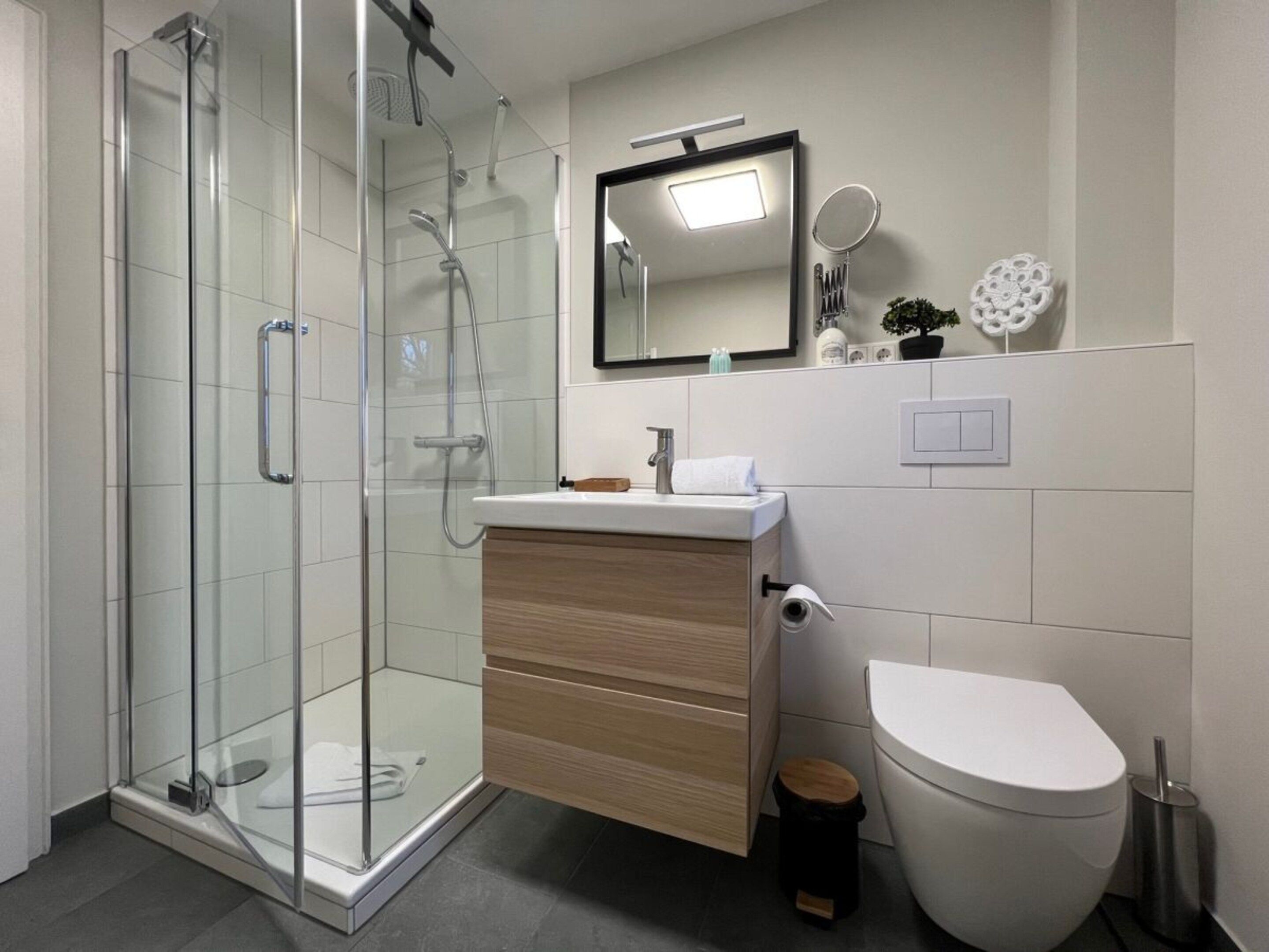 A modern bathroom with a glass-enclosed shower, a wooden vanity, a white toilet, and a mirror above the sink.