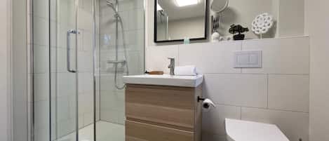 A modern bathroom with a glass-enclosed shower, a wooden vanity, a white toilet, and a mirror above the sink.