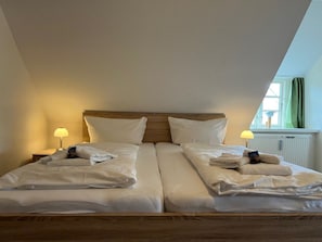 Ein Doppelzimmer mit zwei Betten, einem Holzkopfstück, Nachttischlampen und einem Fenster mit Vorhängen.