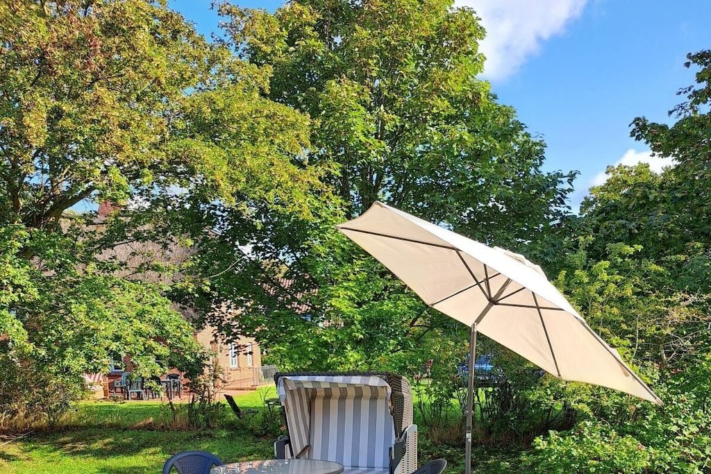 An outdoor seating area with a table and chairs, a striped umbrella, and lush greenery.