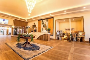 Eine Hotelhalle mit einer Rezeption, einer Kristallleuchter und gerahmten Kunstwerken.