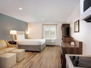 Habitación de hotel con cama, escritorio, televisión, silla y pequeña kitchenette.