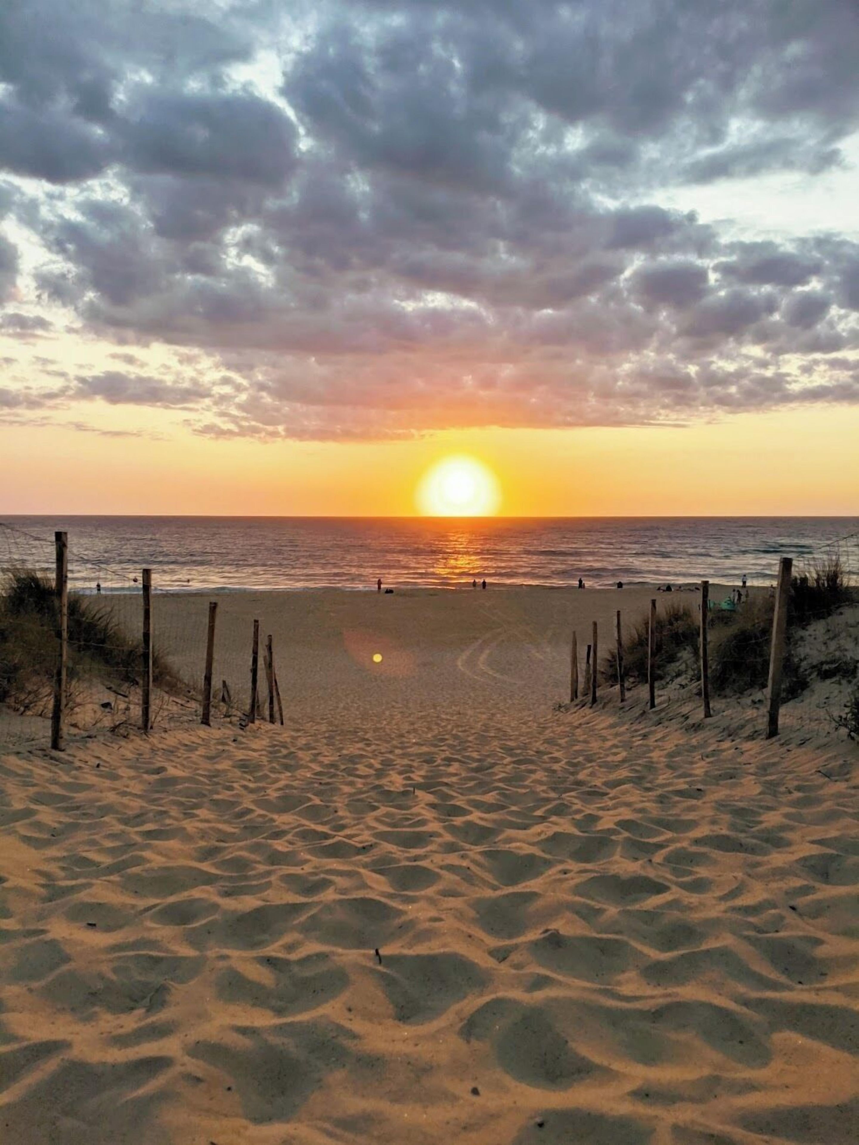 A beach with a fence in the foreground and the sun setting over the ocean.