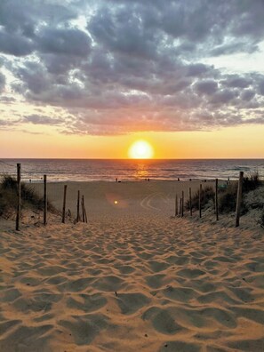 A beach with a fence in the foreground and the sun setting over the ocean. - Nahia: Premium apartment with parking, near Lake Hossegor and the ocean (Seignosse)