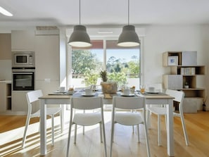 A modern kitchen with white cabinetry, a built-in microwave, and a dining area with a table set for four. - Nahia: Premium apartment with parking, near Lake Hossegor and the ocean (Seignosse)
